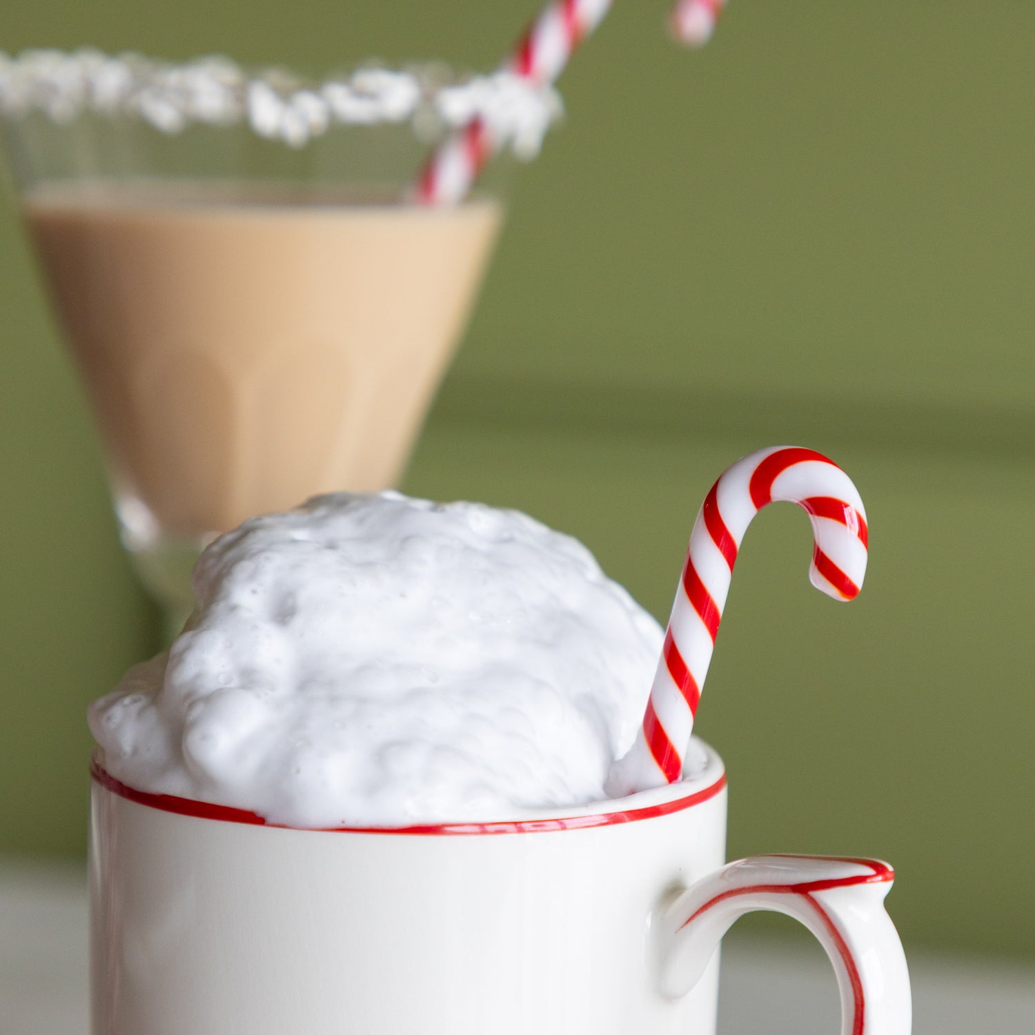 Mug with whipped cream and a candy cane stir stick on a green background.