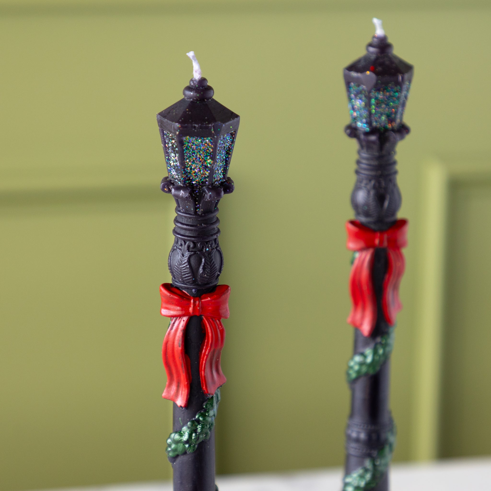 Decorative candlesticks resembling street lamps with red bows on a green background.