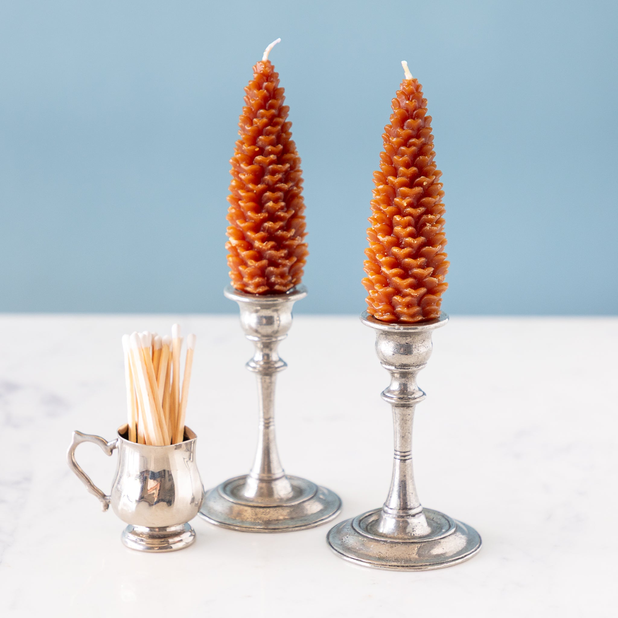 Two cone-shaped candles in silver candlesticks on a light surface with a blue background.