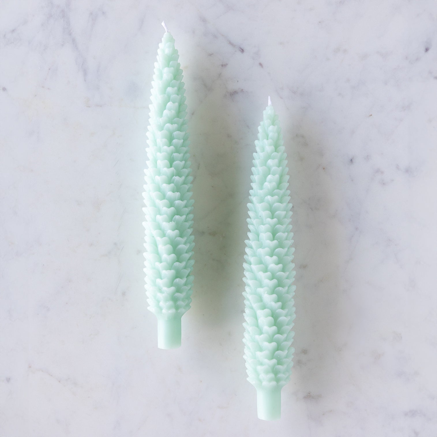 Two Mint Large Pinecone Taper Candles on a marble table.