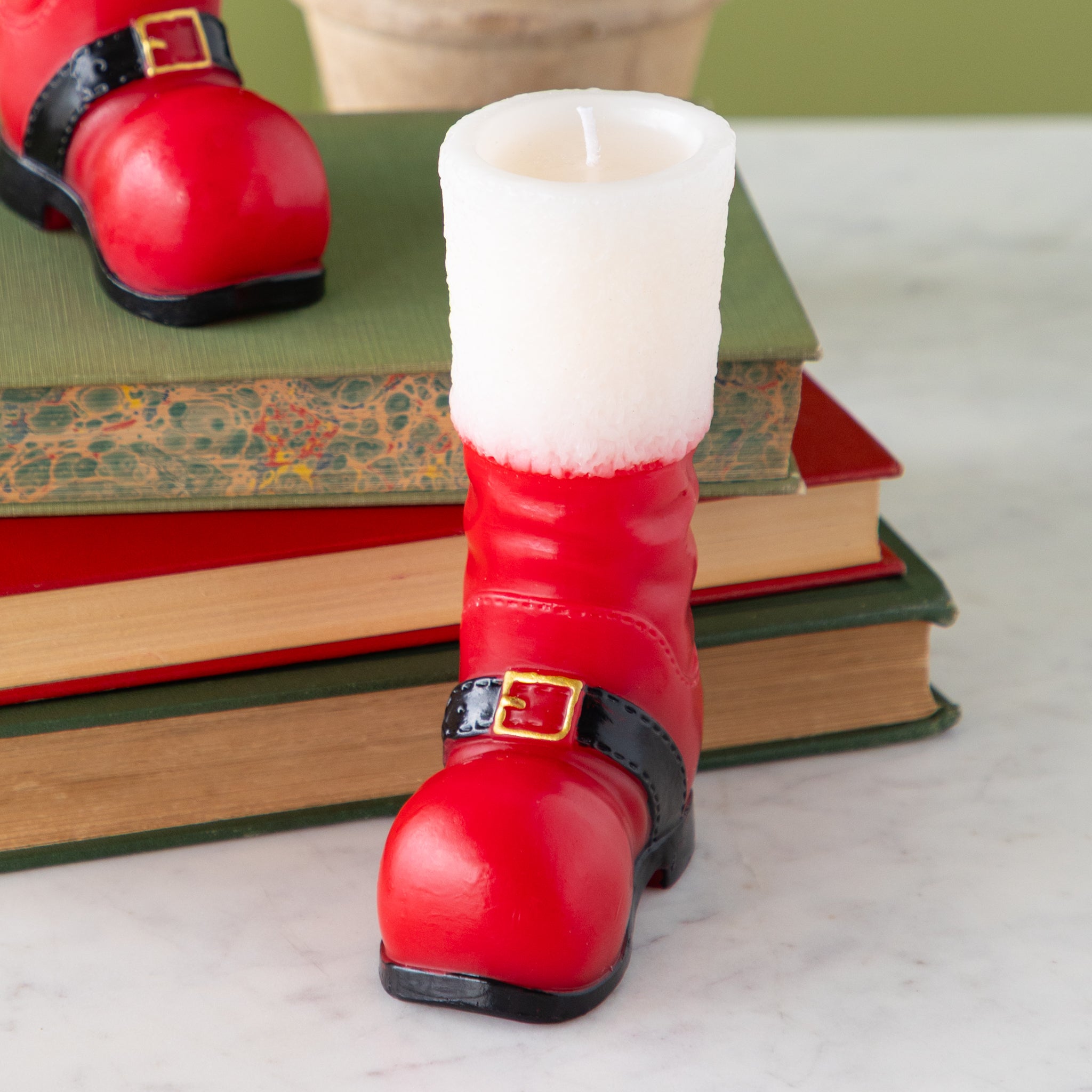 A close up of the Santa Boot Shaped Candle in front of a stack of books.