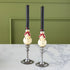 Two Snowman Taper Candles in vintage candlestick holders on a marble table against a green wall.