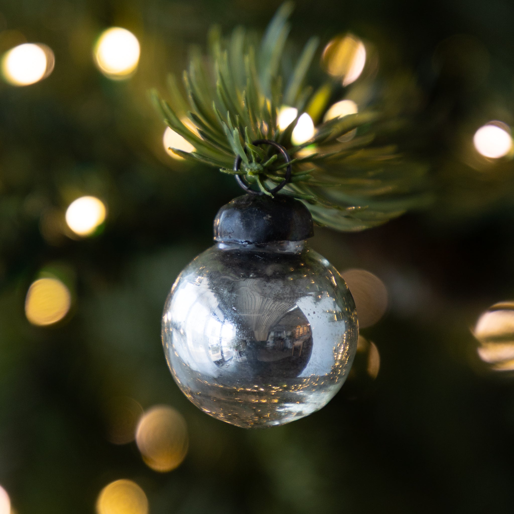 Silver Ball Mercury Glass Ornament hanging on a lit Christmas tree.