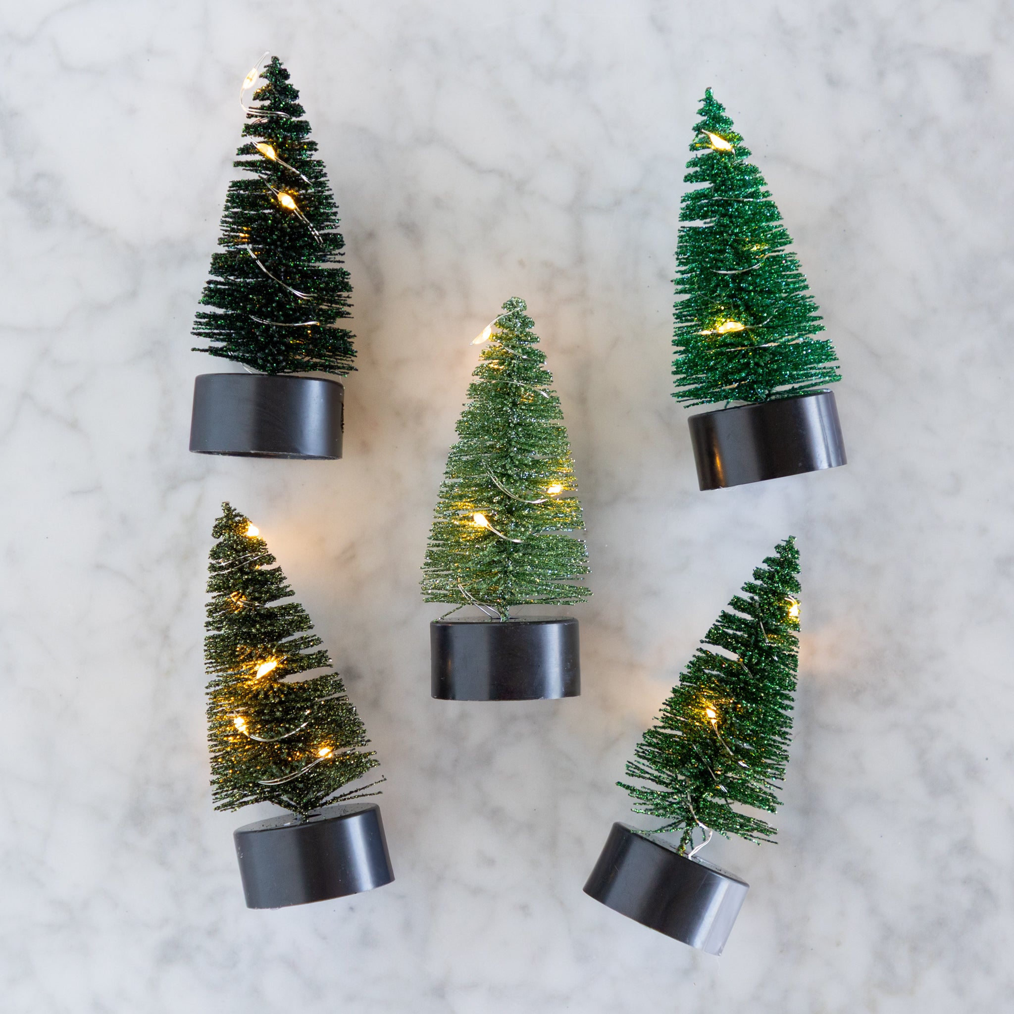 Five small pre-lit bottle brush trees on a marble surface.