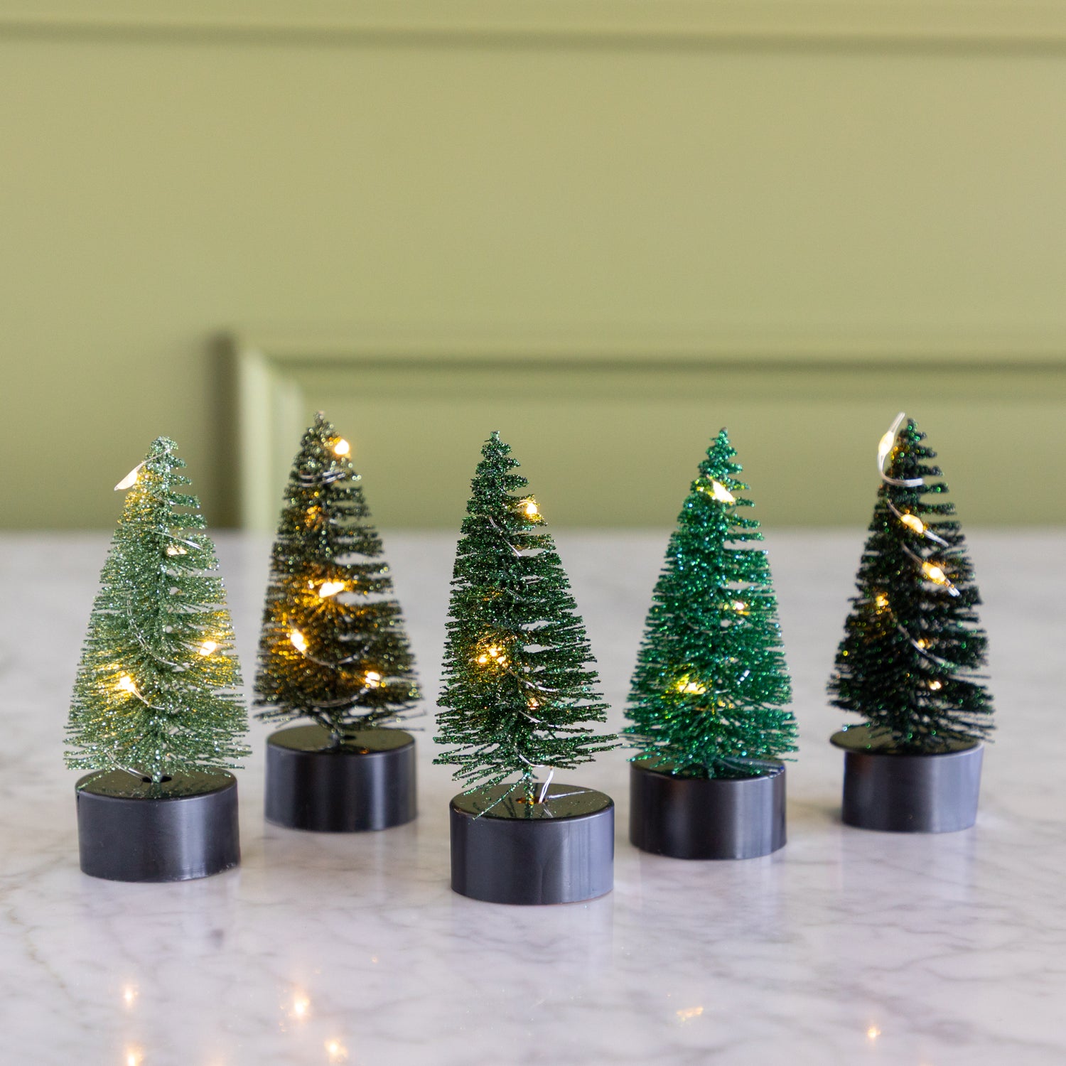 Five small pre-lit bottle brush trees on a marble surface.