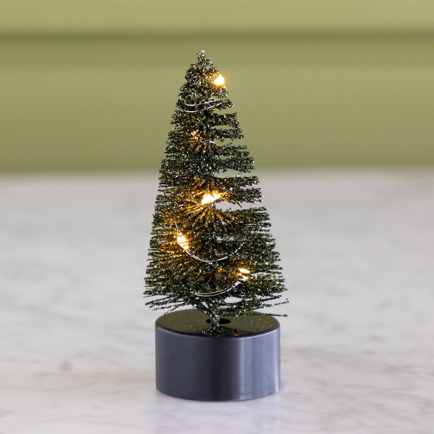 Small dark green bottle-brush tree with lights on a neutral background.
