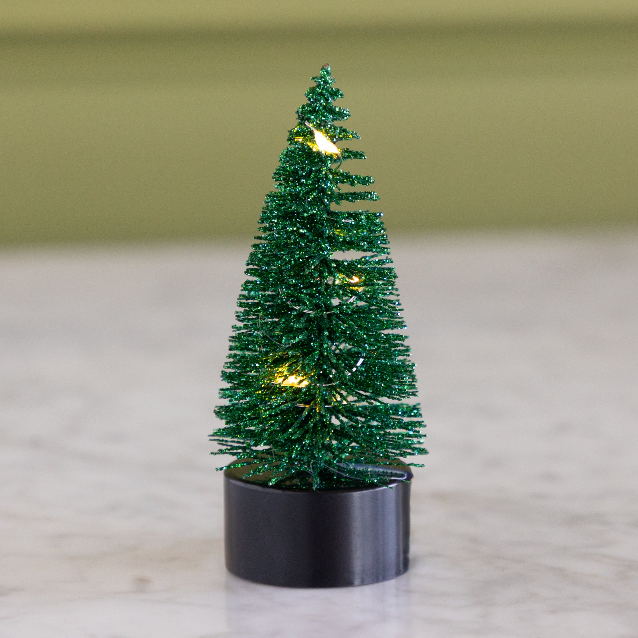 Small bright green bottle-brush tree with lights on a neutral background.