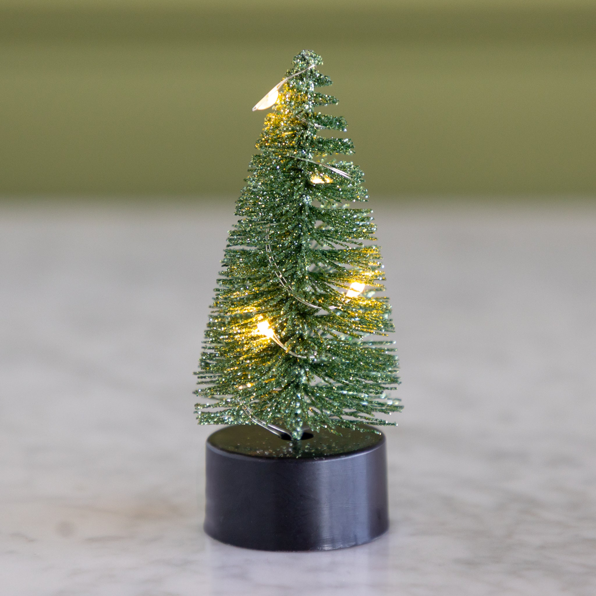 Small light green bottle-brush tree with lights on a neutral background.