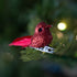 Red glittery bird ornament on a branch with blurred green background.