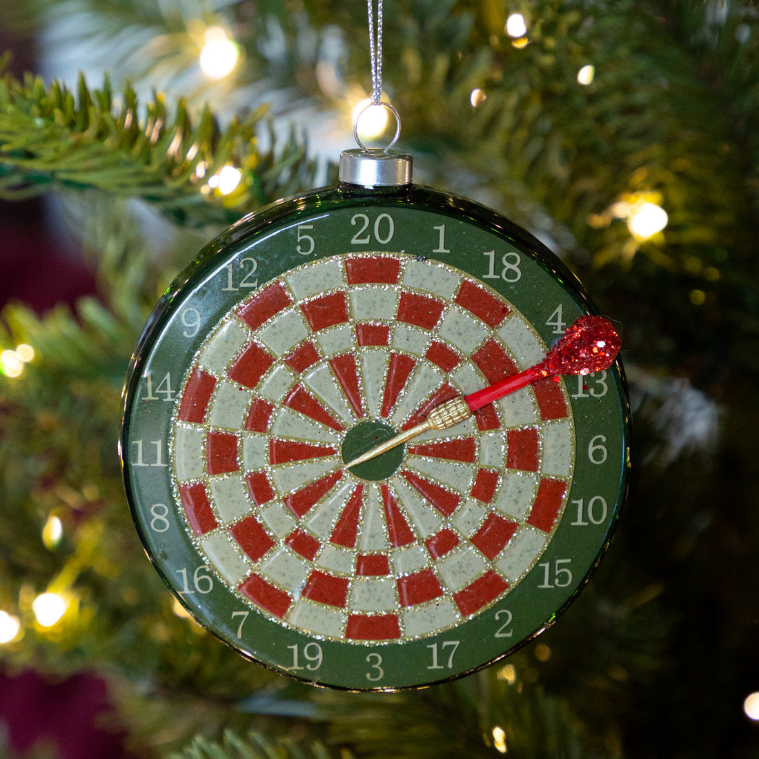 Dartboard ornament with a red dart on a Christmas tree.
