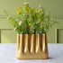 Tall Aluminum Gold Wave vase with greenery on a light surface against a green wall.