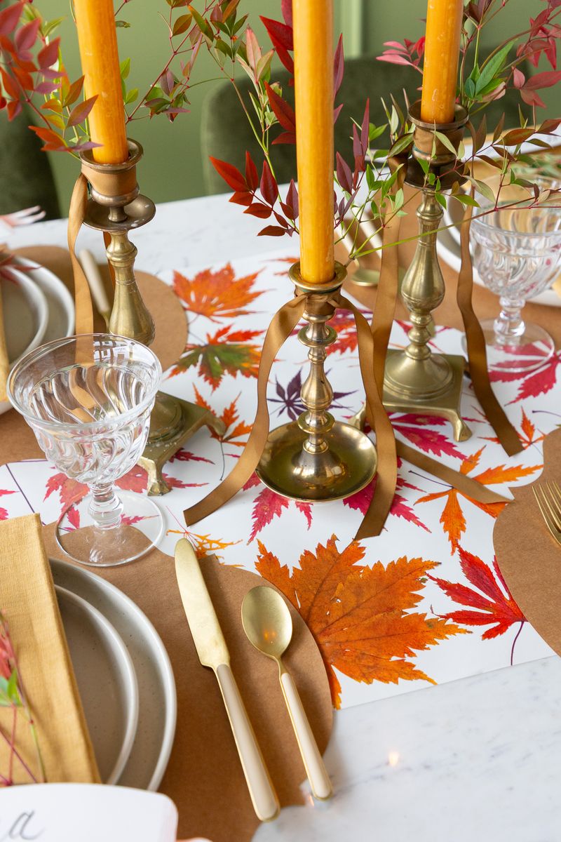 Decorative table setting with fall-themed tablecloth, candles, and cutlery.