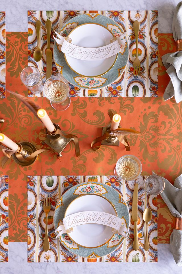 Decorative table setting with ornate plates, gold cutlery, and candles on a patterned tablecloth.