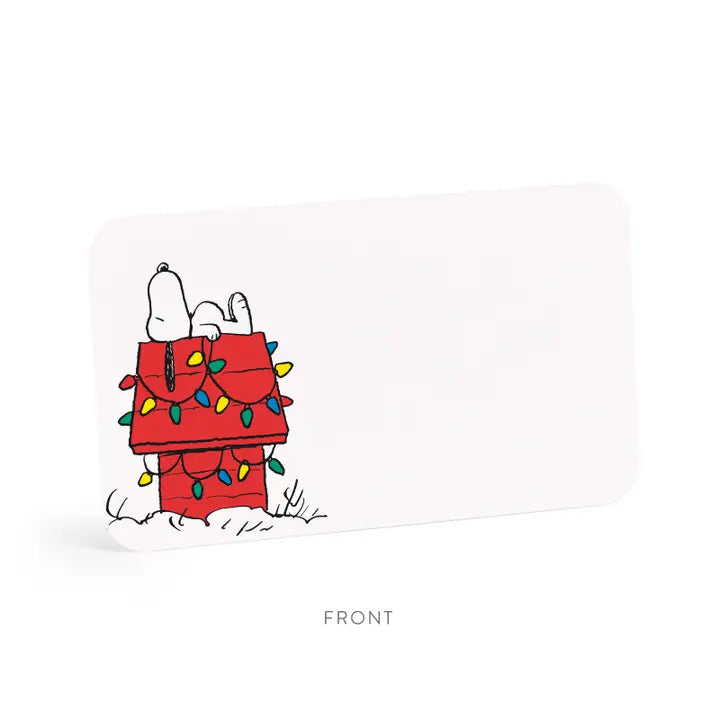 A white rectangular product card or packaging insert with rounded corners, shown on a white background. The front features a small illustrated graphic of Snoopy lying on top of a red dog house decorated with colorful Christmas lights.