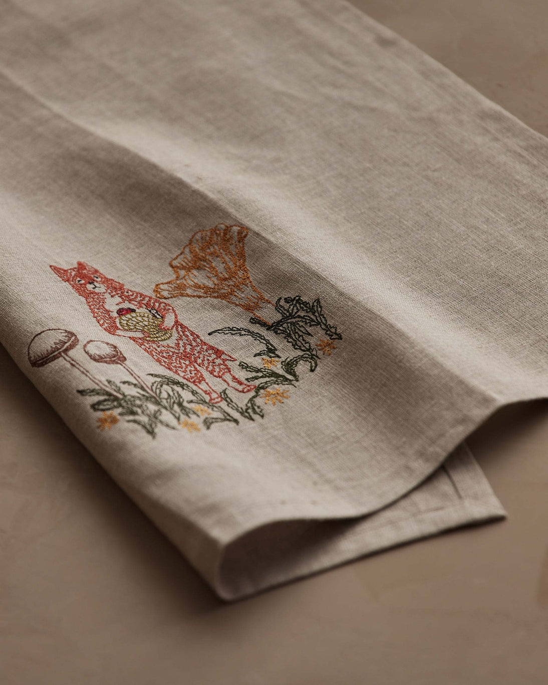 Embroidered fabric with a design of a fox and plants on a beige background.