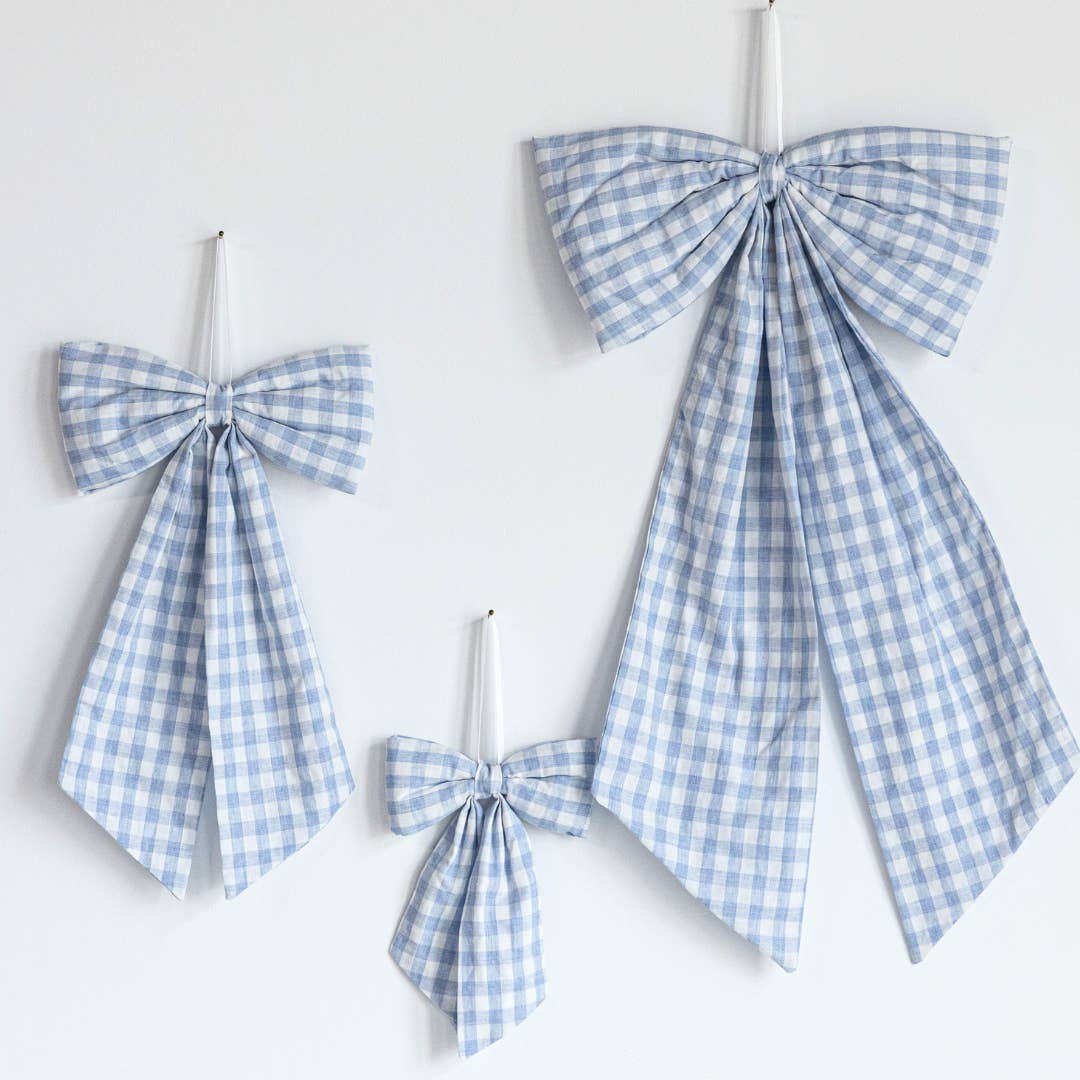 Three blue and white gingham bow decorations of different sizes hanging on a plain white wall.