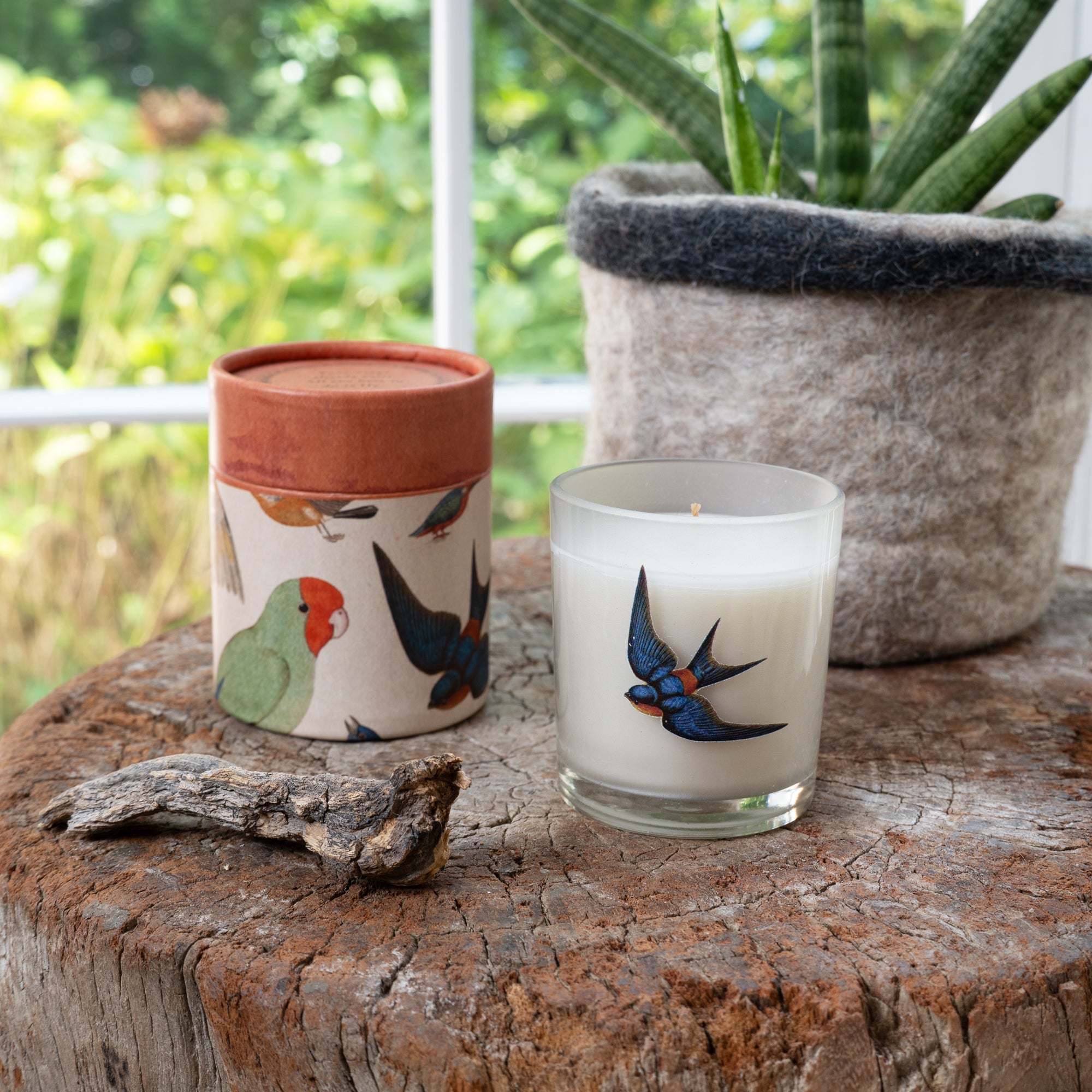 Two candles with bird designs on a wooden surface outdoors.