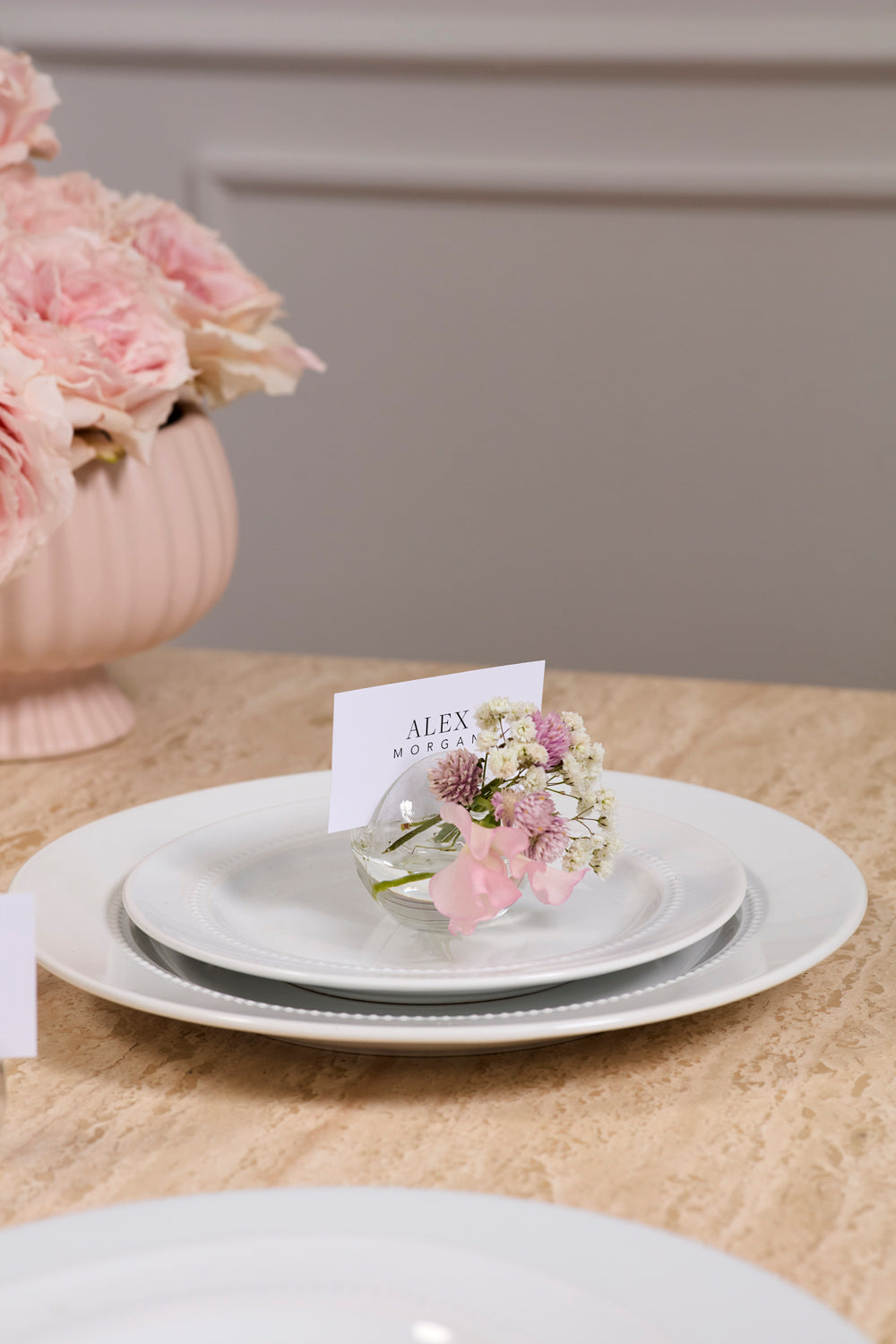 Table setting with floral arrangement and place card on a beige tablecloth.
