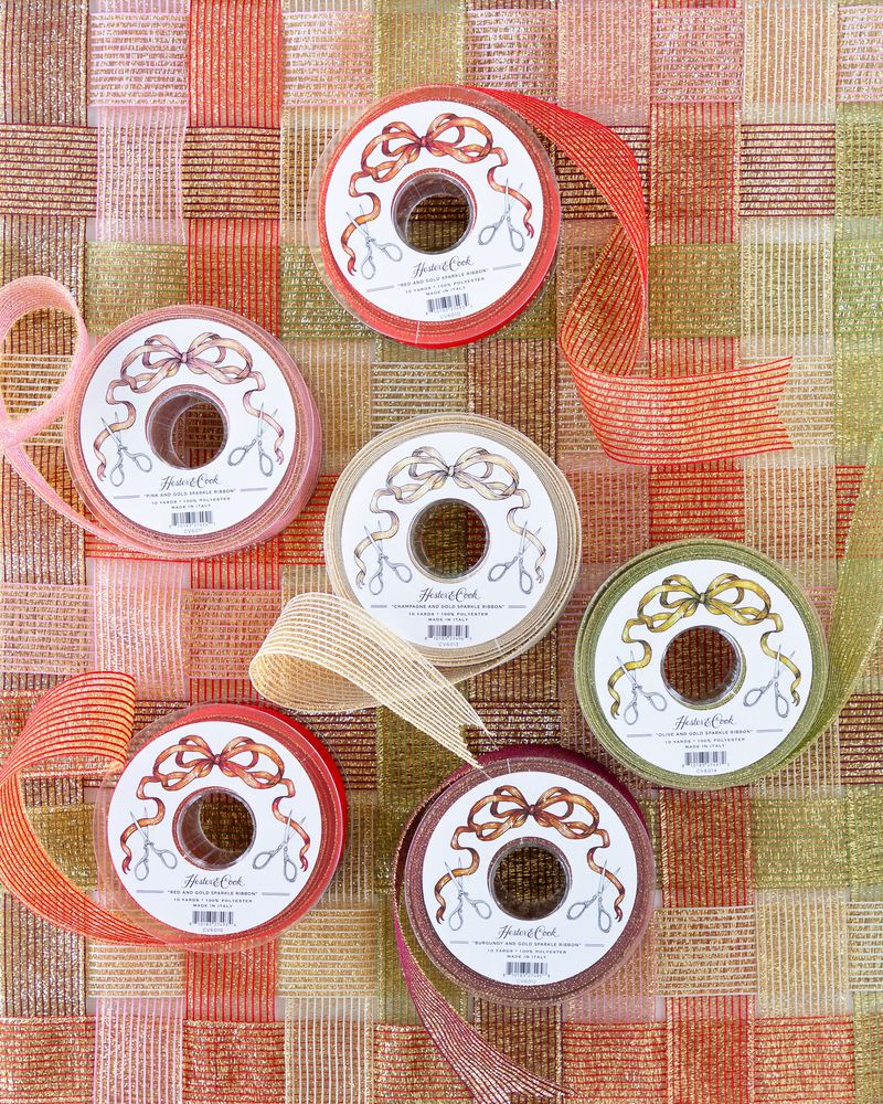 Several spools of sparkly ribbon in various colors unraveled on a surface of woven sparkle ribbon. 

