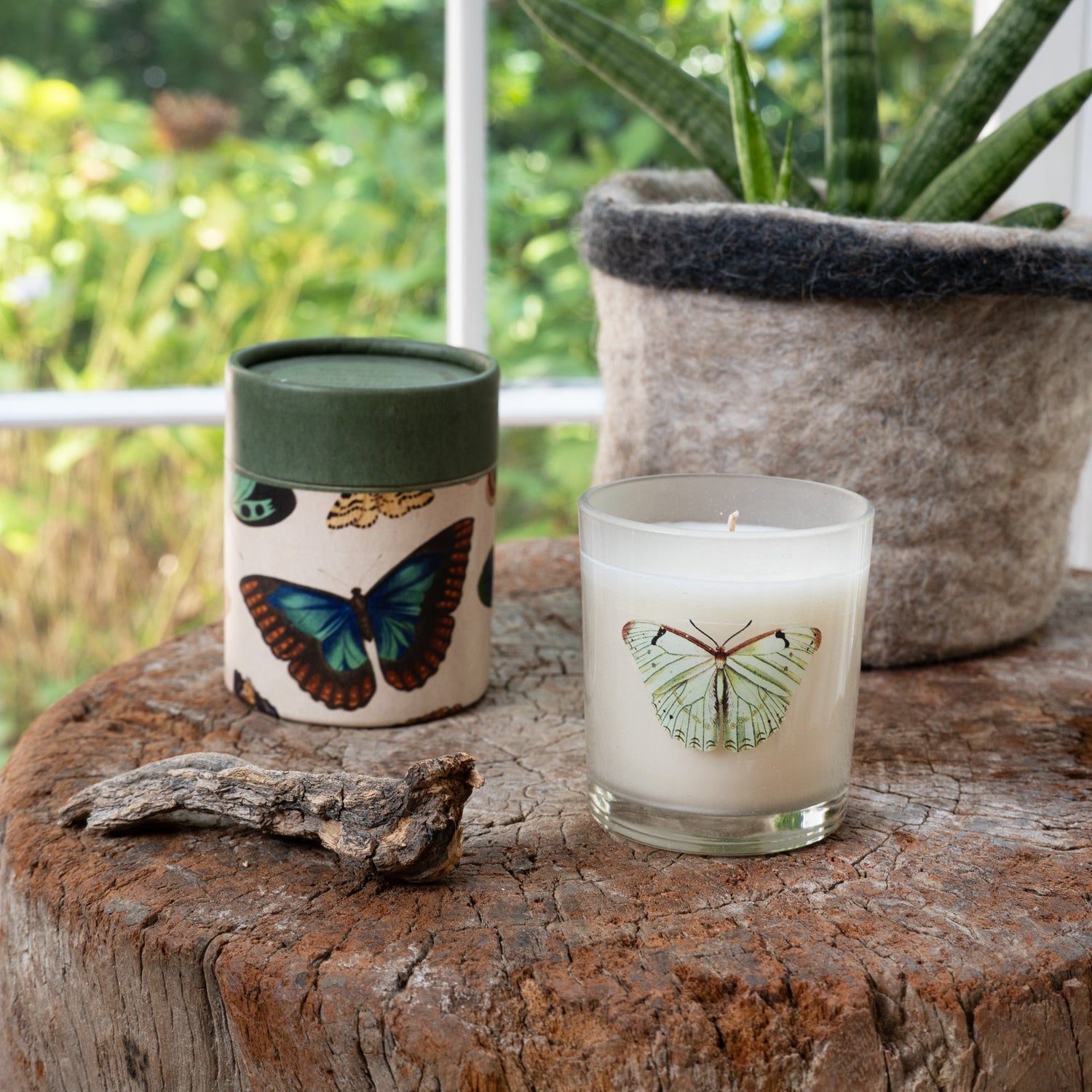 Two candles with butterfly designs on a wooden surface outdoors.