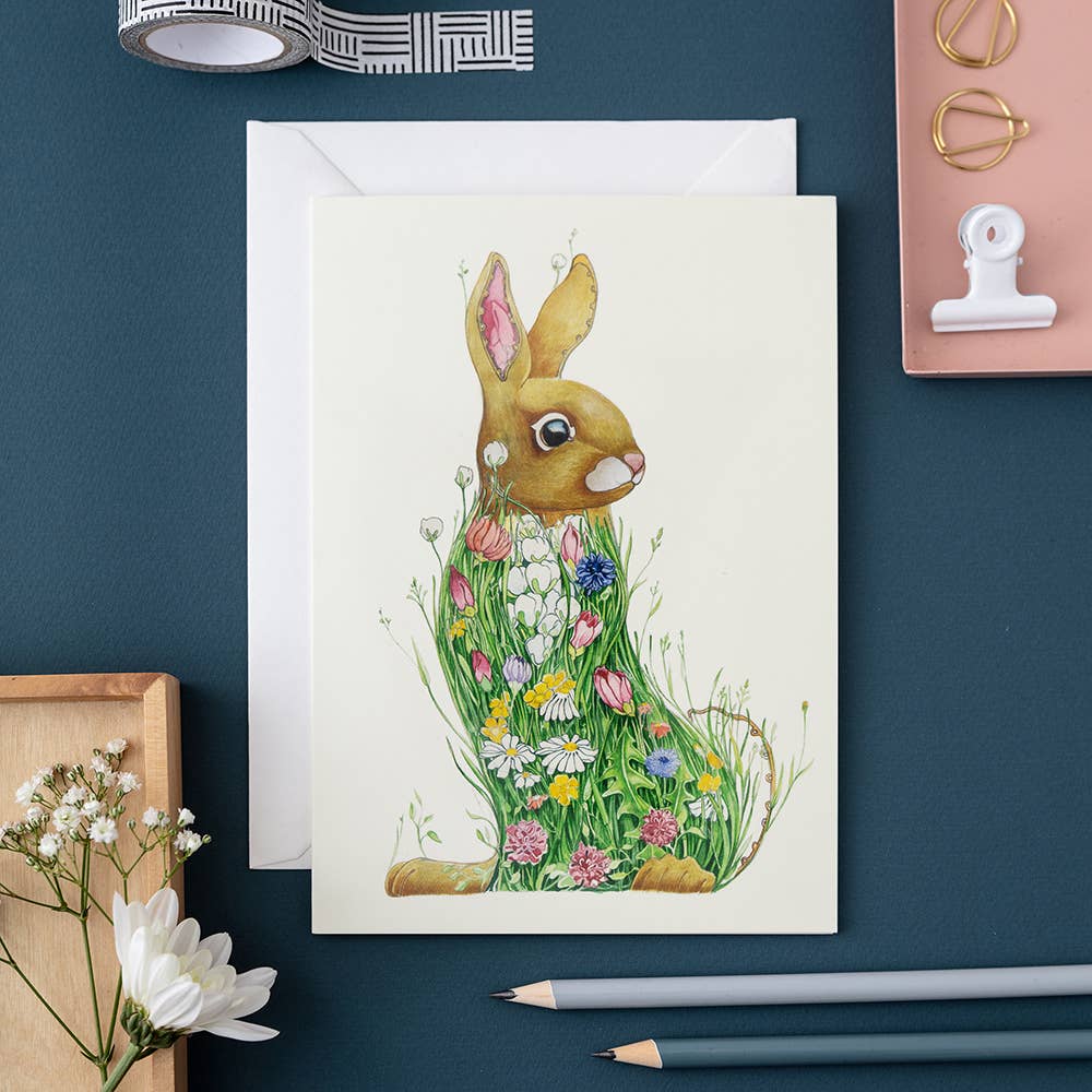 Greeting card with a rabbit illustration on a blue surface with stationery items.