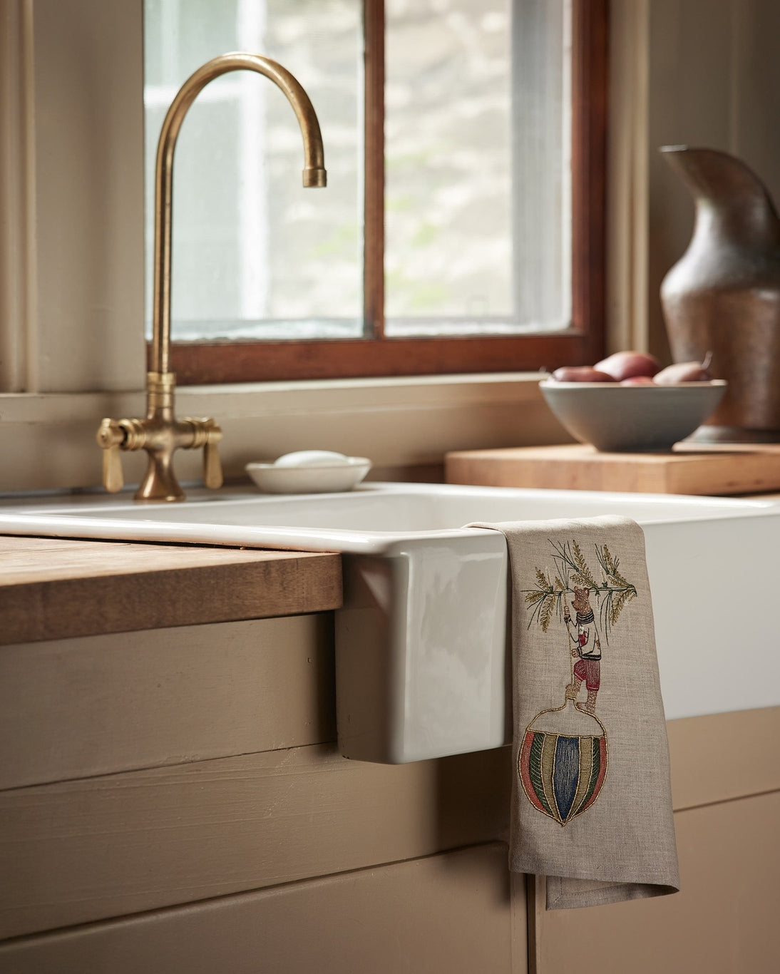 Kitchen sink area with a decorative towel, soap, and window in the background