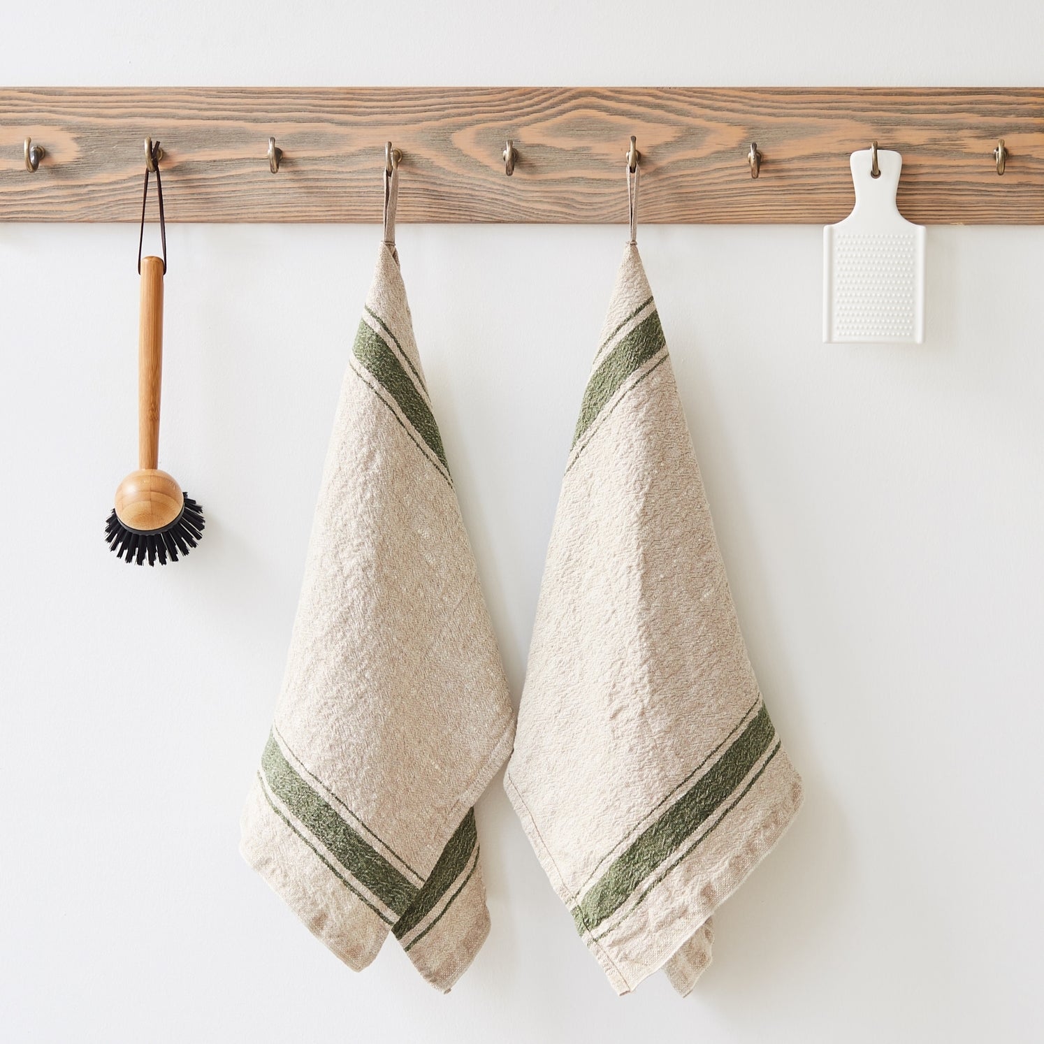 Two beige towels with green stripes hanging on a wooden rack against a white wall.