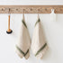 Two beige towels with green stripes hanging on a wooden rack against a white wall.