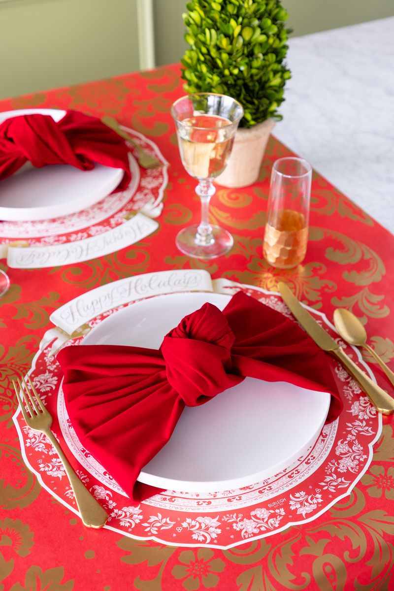 A holiday place setting with a wide soft red ribbon tied like a bow around the plate. 