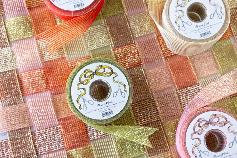 Several spools of sparkly ribbon in various colors unraveled on a surface of woven sparkle ribbon. 
