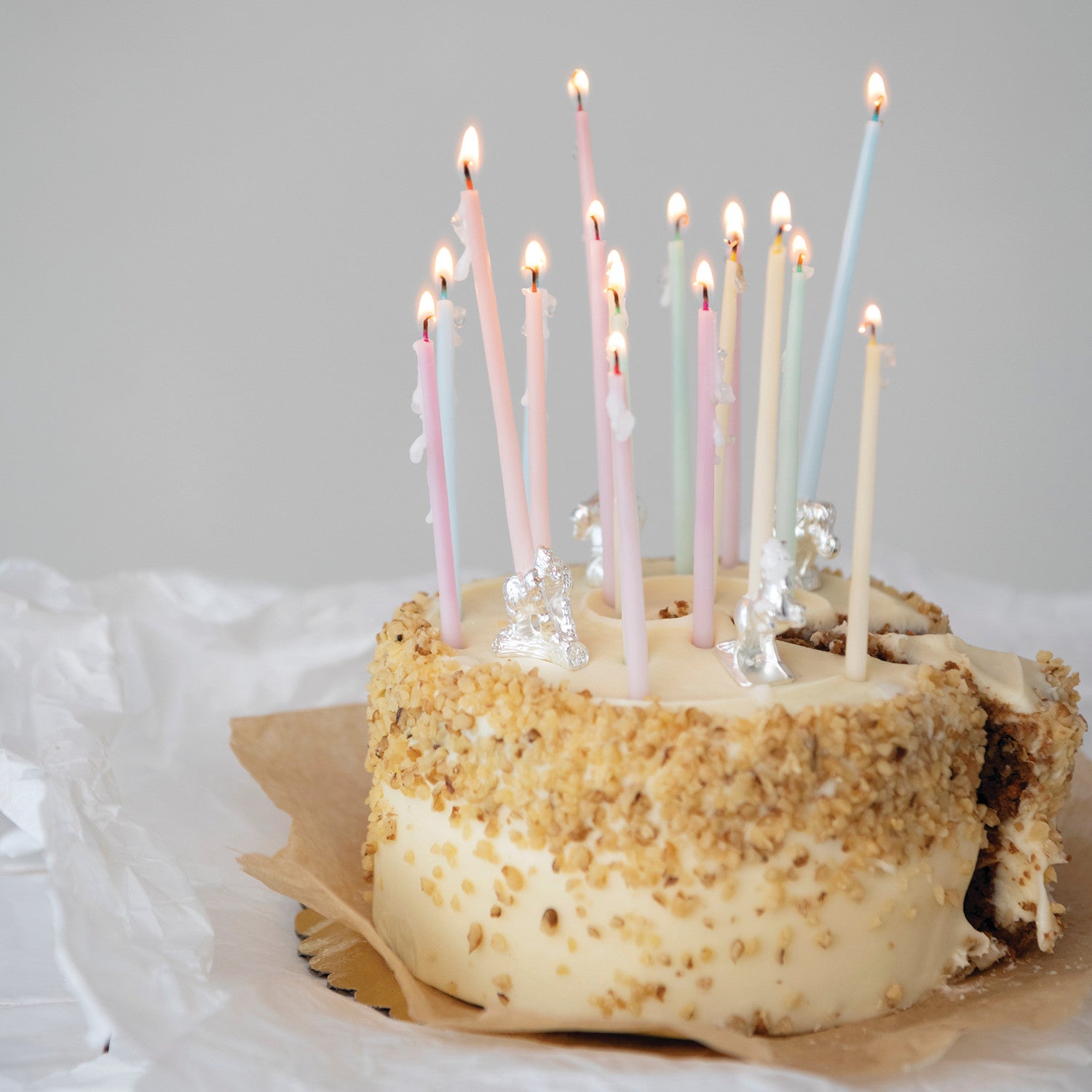 Small round cake with white frosting and brown crumbly top, decorated with lit candles on a light gray background.
