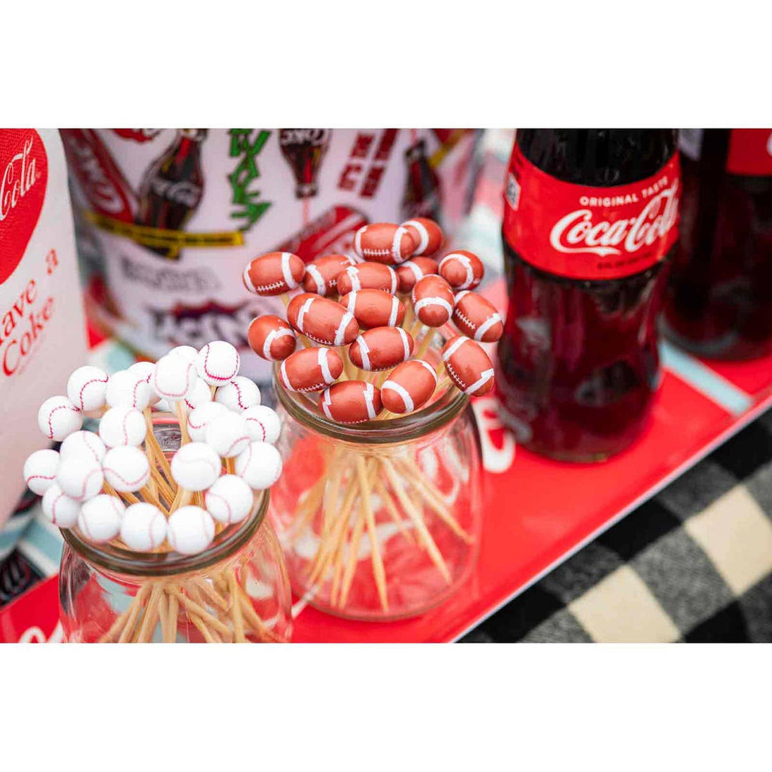 Two jars with football and baseball picks,  on a Coca-Cola branded tray.