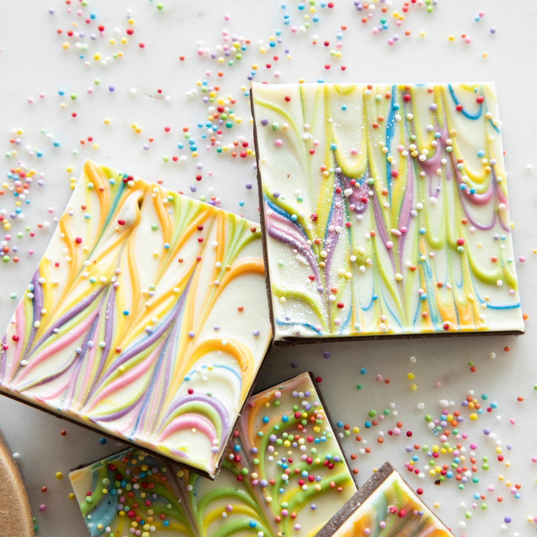 Four squares of Hester &amp; Cook Rainbow Bark with rainbow sprinkles on top.