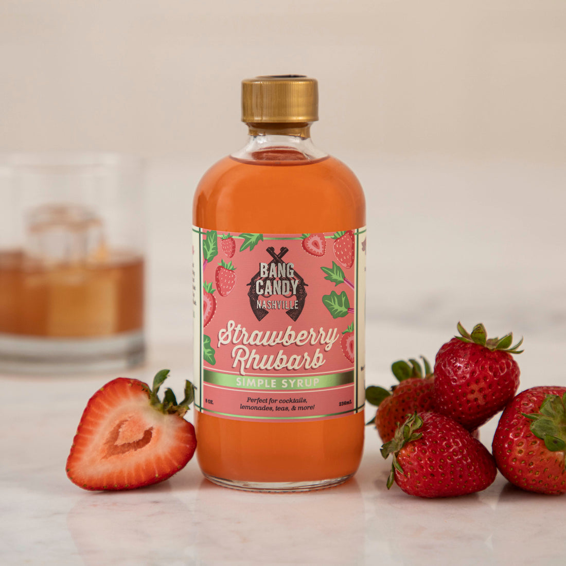 A bottle of Hester &amp; Cook Strawberry Rhubarb Syrup with strawberries next to it, perfect for creating refreshing Pimms Cup cocktails or summer sodas.