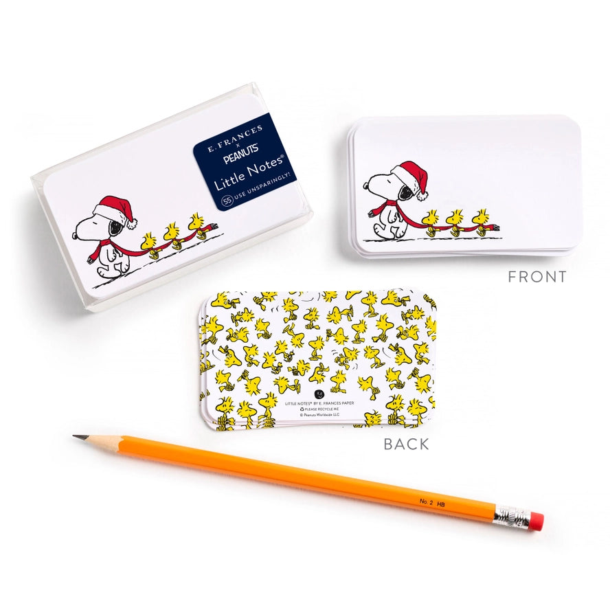 Three white rectangular notebook covers with Peanuts Snoopy and Woodstock holiday illustrations are arranged on a white background, along with an orange pencil. Two covers are labeled FRONT and one is labeled BACK; one front view shows a dark blue label reading &