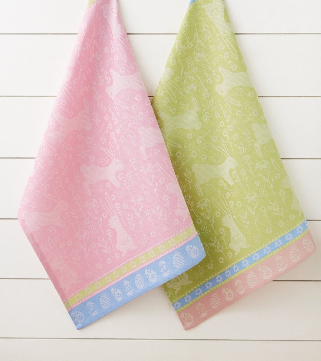 Two patterned towels, one pink and one green, on a white wooden surface.