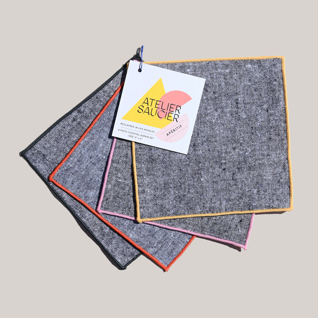 A set of four rainbow chambray cocktail napkins with colored edges laid out flat.