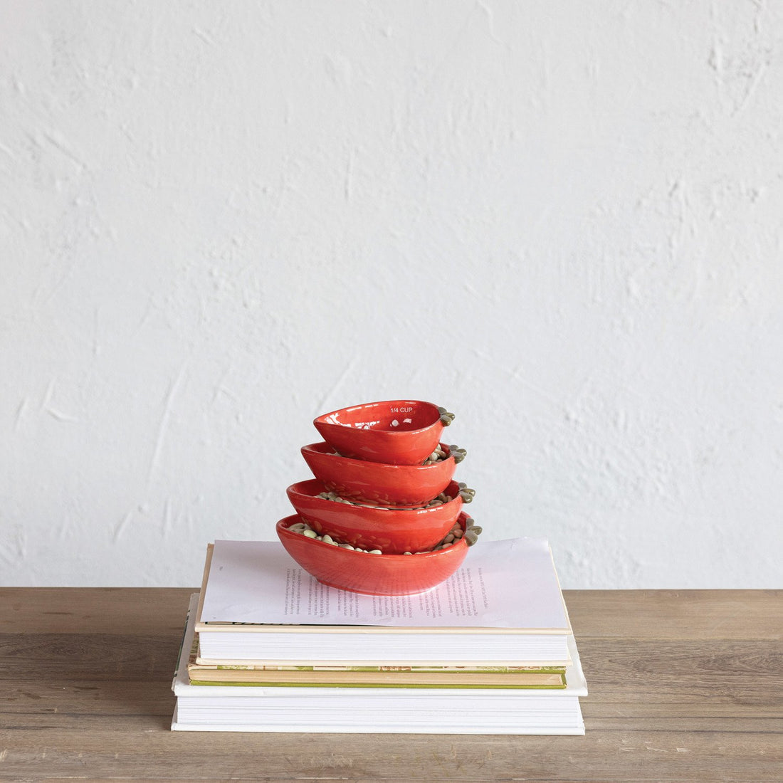 Set of red strawberry shaped measuring cups stacked on a stack of books with a white background.