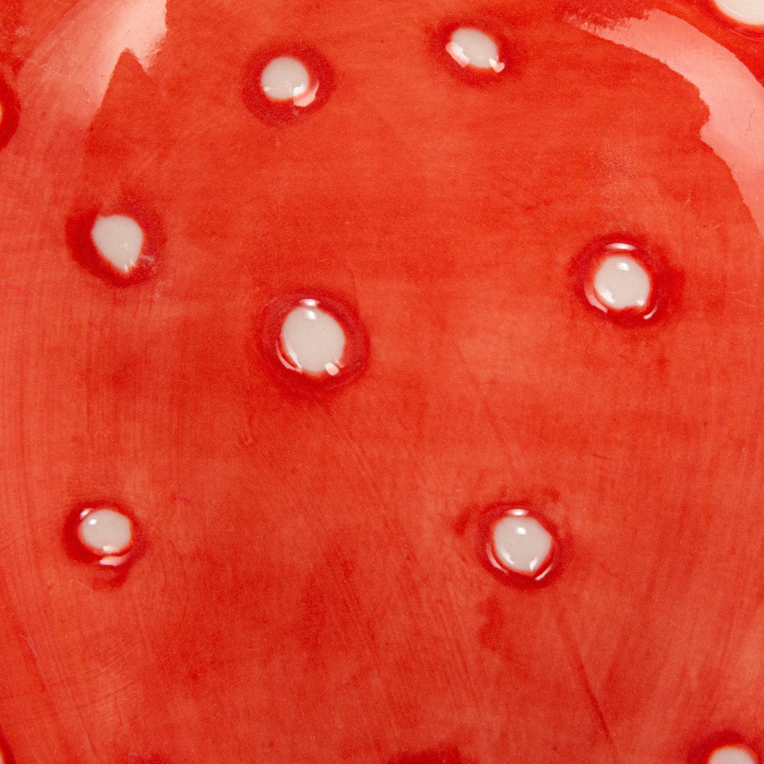 Close-up of a red strawberry  ceramic measuring cup with white seeds painted on it. 