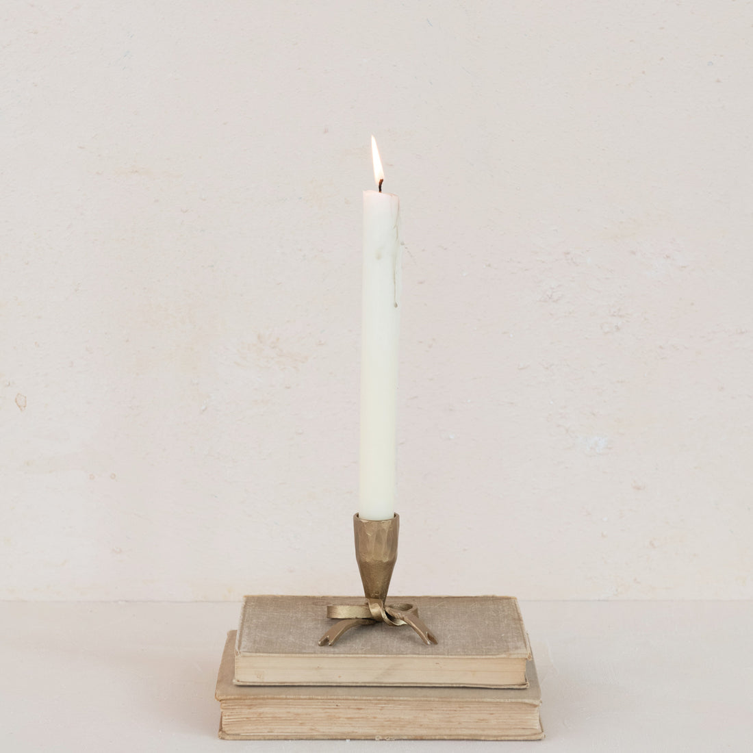 Candle in a decorative holder on top of stacked books against a plain background.
