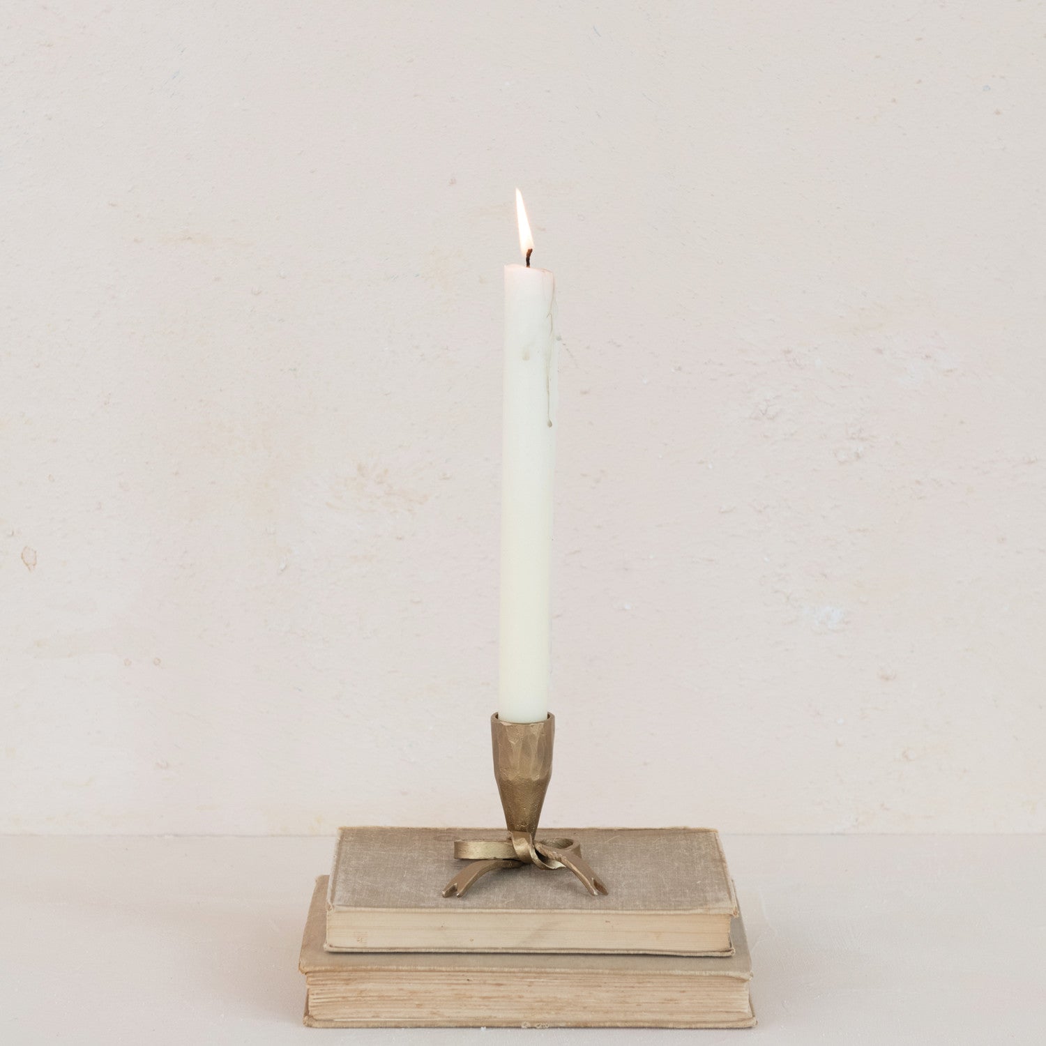 Candle in a decorative holder on top of stacked books against a plain background.