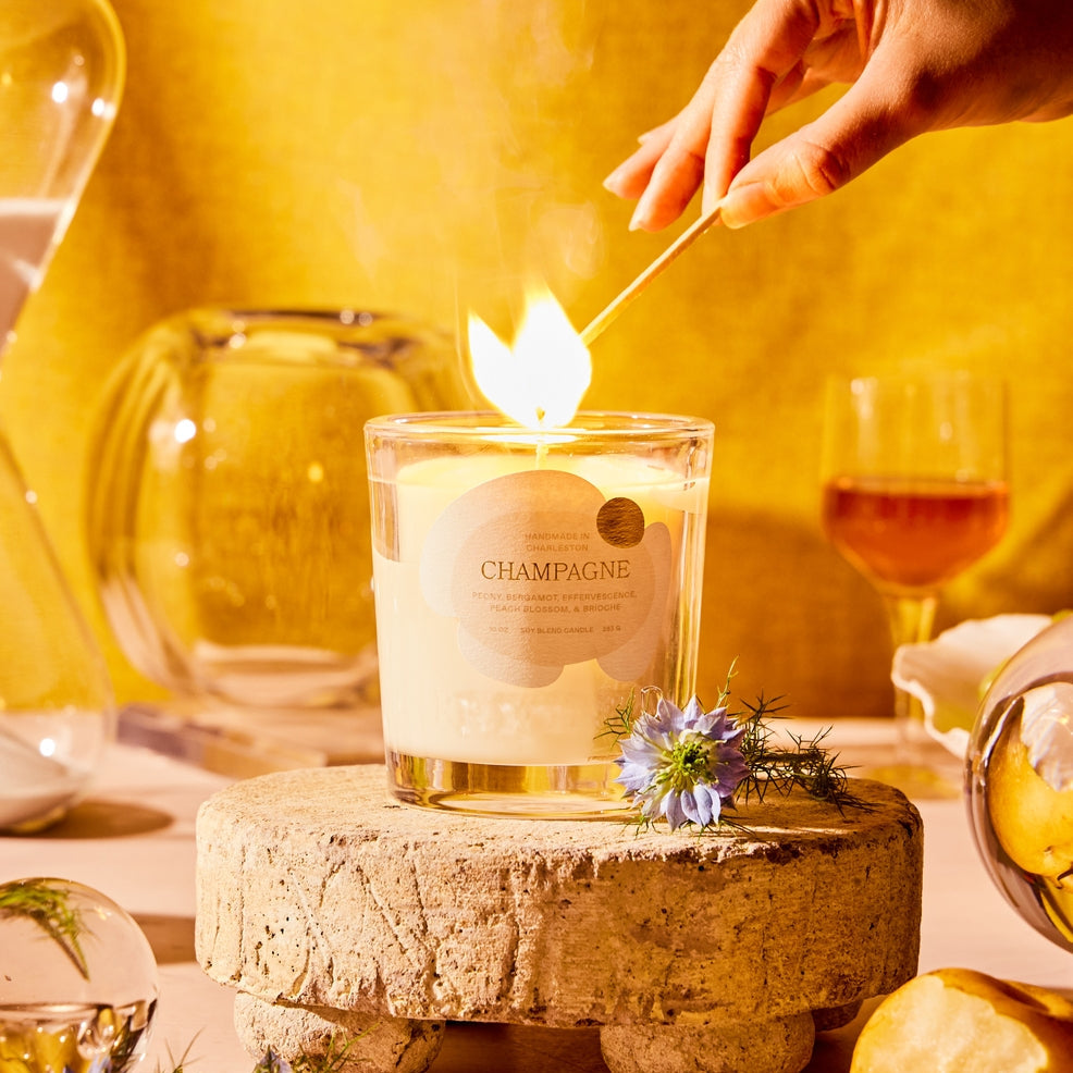 Candle being lit with a match on a decorative stone holder, surrounded by a warm yellow background.