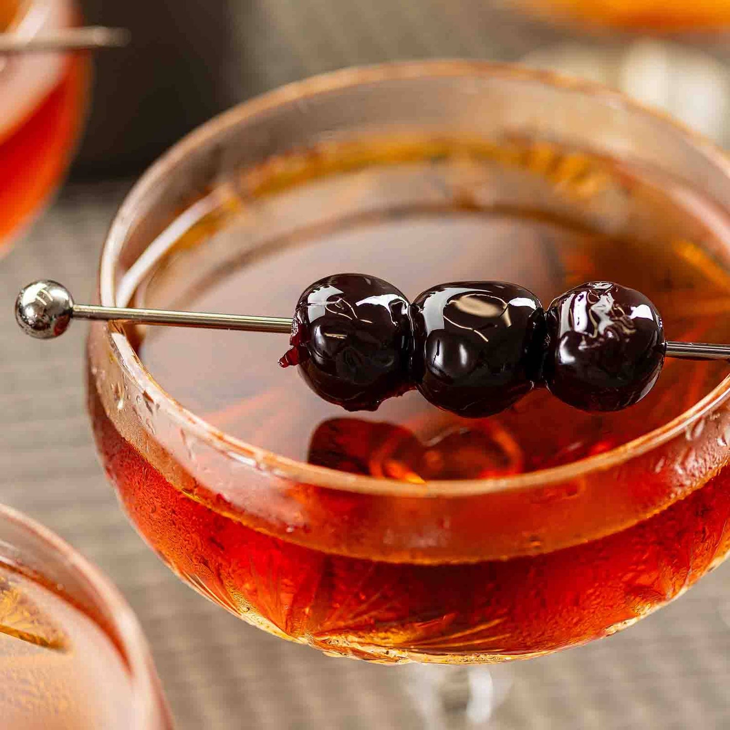 Cocktail with a blueberry and lemon peel garnish in a glass skewed by the Gunmetal Cocktail Pick.