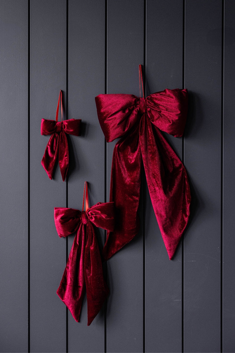 Three red velvet bows hanging on a dark wall.