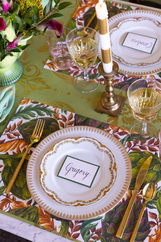 Decorative table setting with place cards, cutlery, and a candle on a colorful tablecloth.