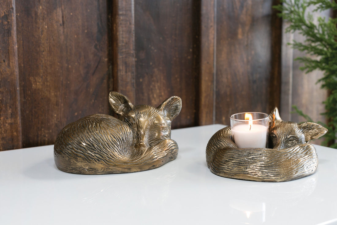Bronze fox-shaped candle holders on a white surface with a wooden background.