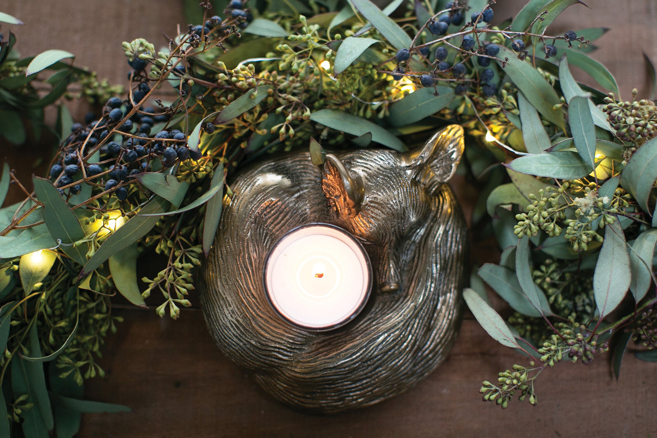 Decorative candle holder shaped like a fox surrounded by greenery and small lights.