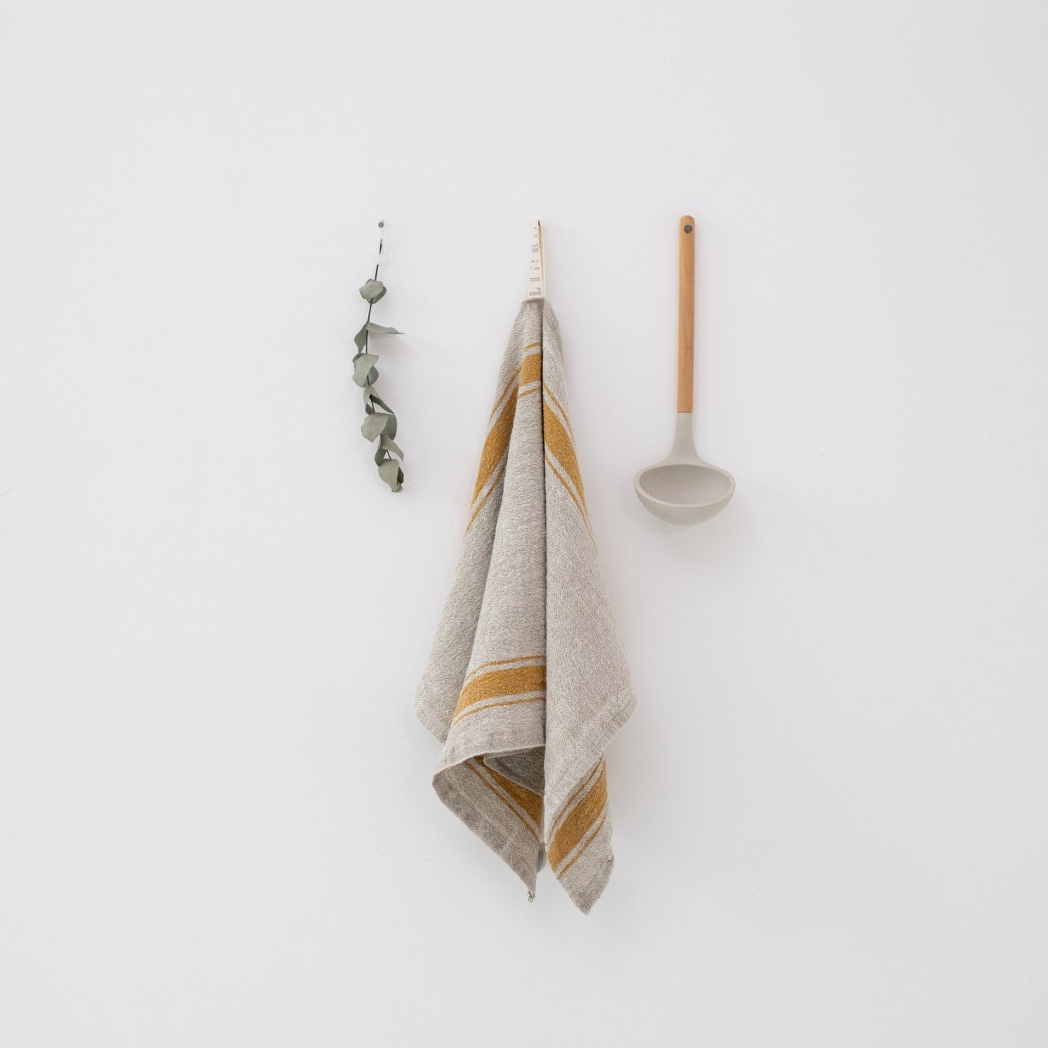 Taupe and yellow striped towel hanging on a white wall with a spoon and decorative item.