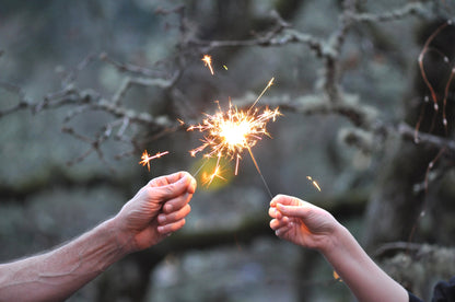 2 hands holding up sparklers to each other. 