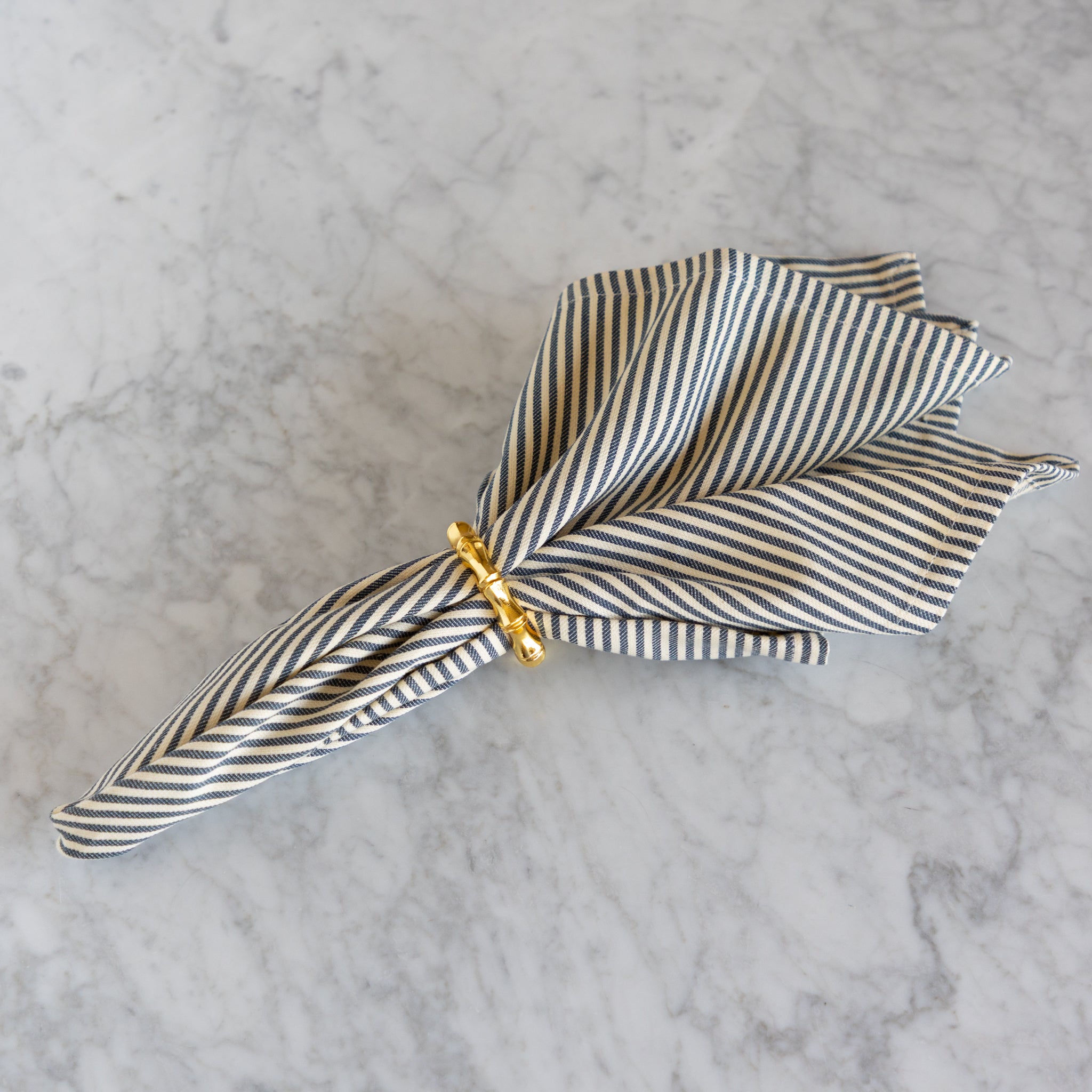 Striped fabric napkin with a gold clip on a marble surface.